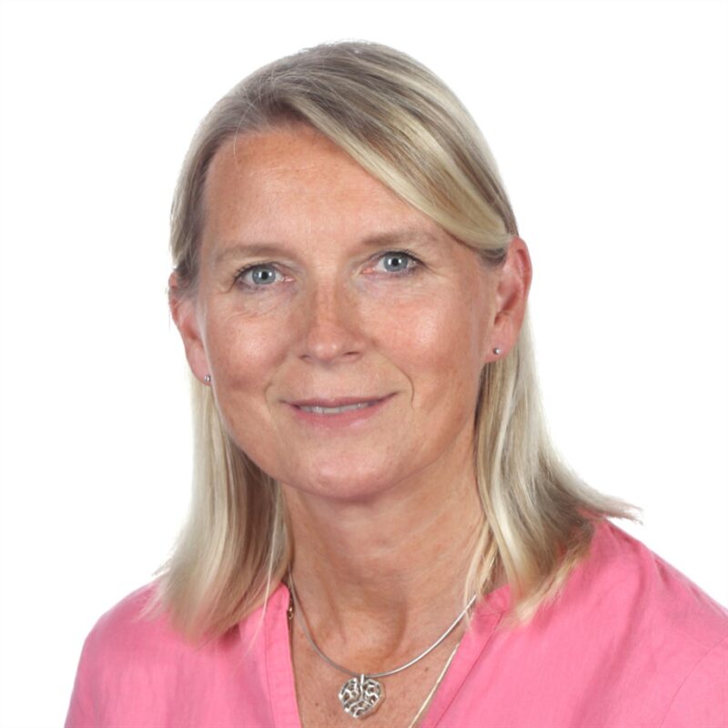 Pitkät vaaleat hiukset omaava henkilö hymyilee kameralle. Heillä on yllään vaaleanpunainen toppi ja sydämenmuotoinen riipus kaulakoru. Tausta on valkoinen.